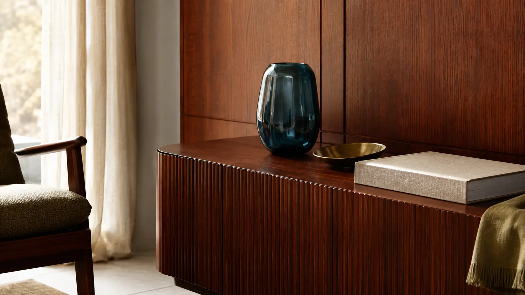 Intérieur contemporain avec meuble en bois acajou, vase pétrole, laiton, livre ivoire et textile olive