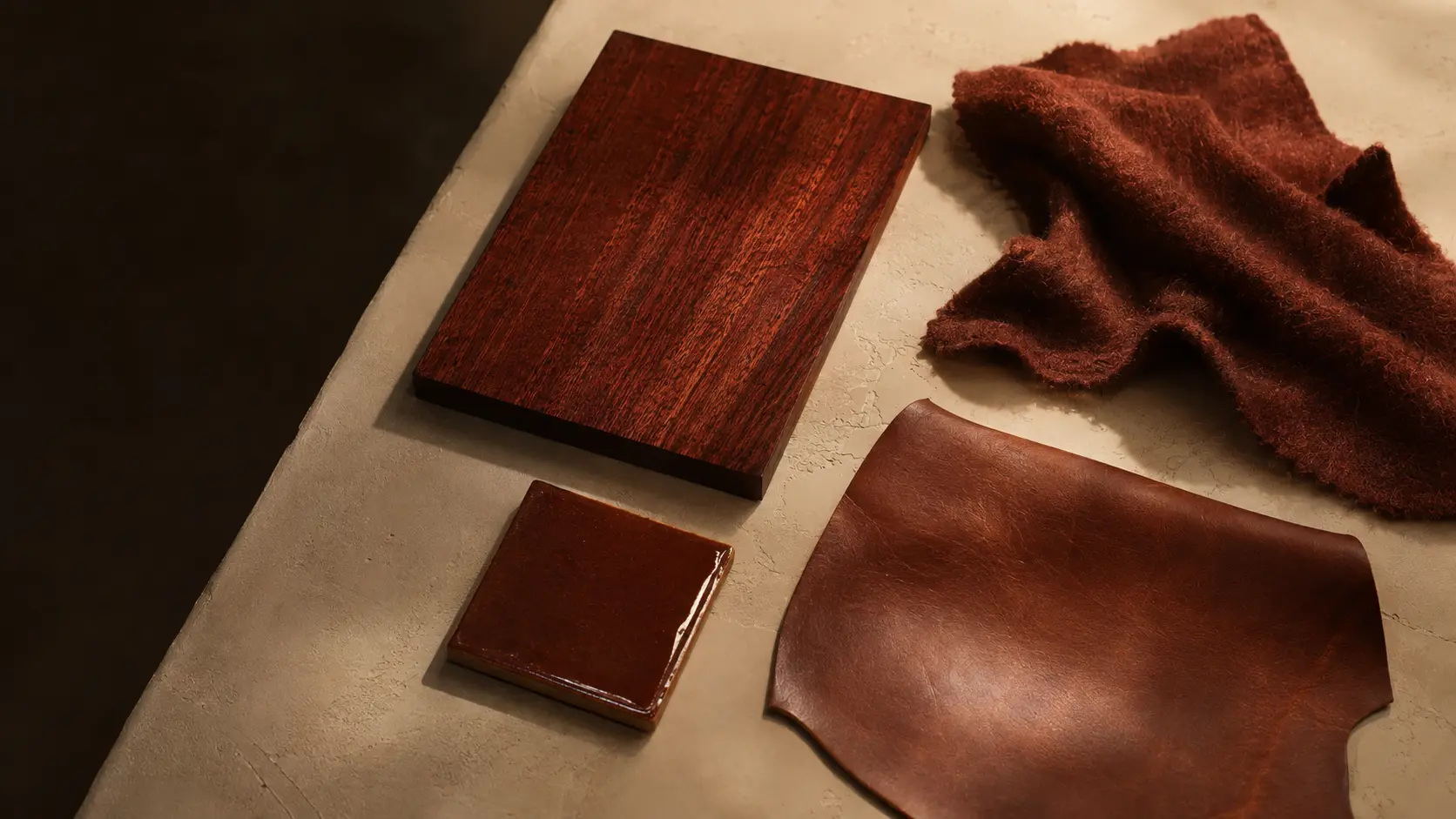 Échantillons acajou de bois verni, textile mat, cuir satiné et céramique brillante sous une lumière latérale