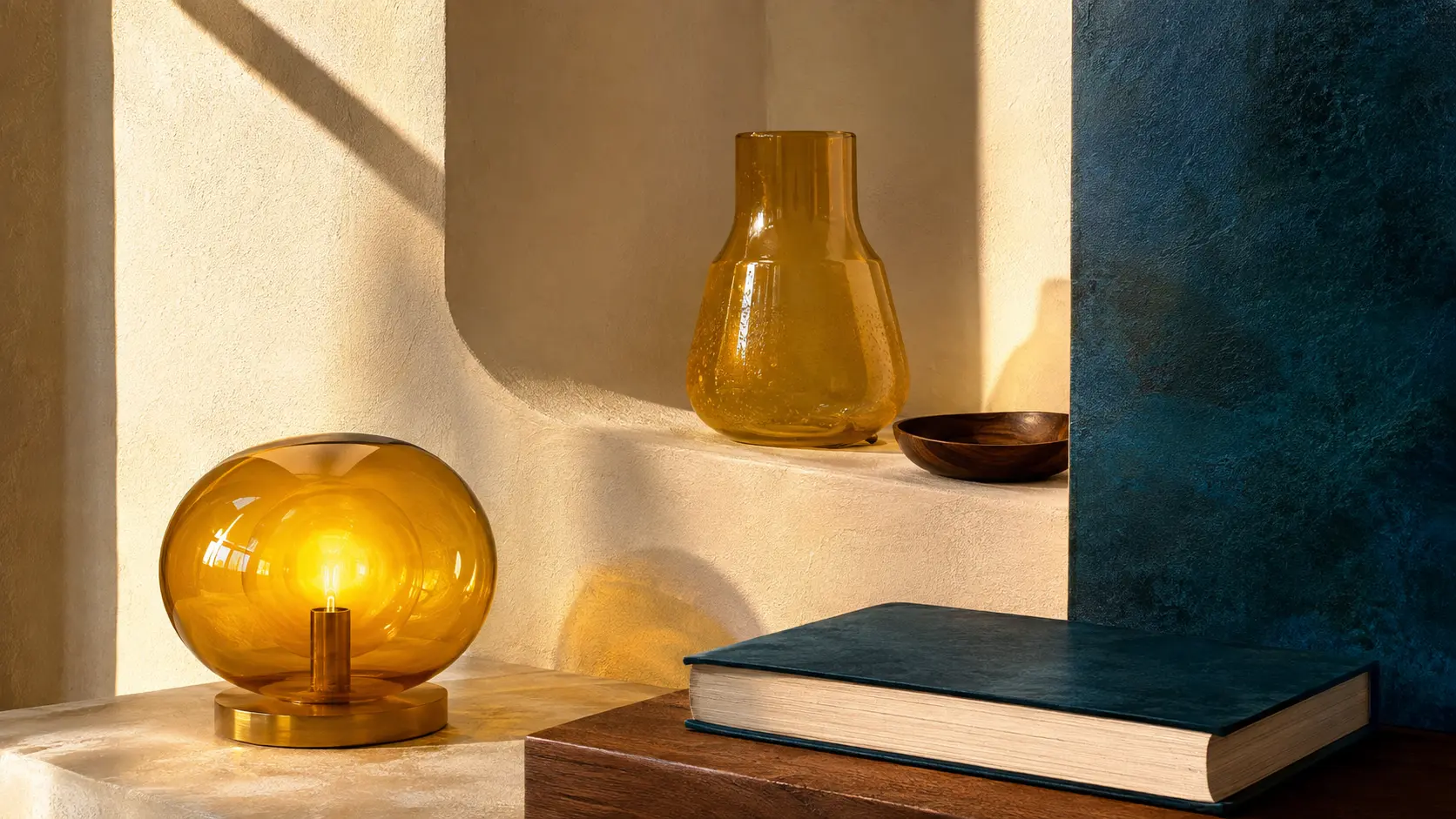 Intérieur lumineux avec lampe et verre ambrés, livre bleu pétrole, ivoire et bois sombre