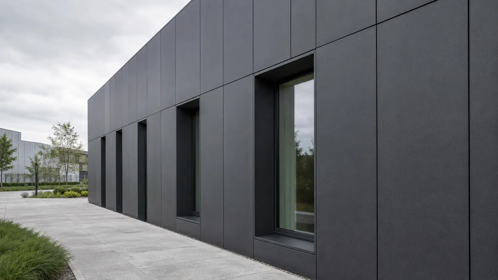 Façade en panneaux métalliques anthracite sous un ciel couvert, avec joints et reflets visibles