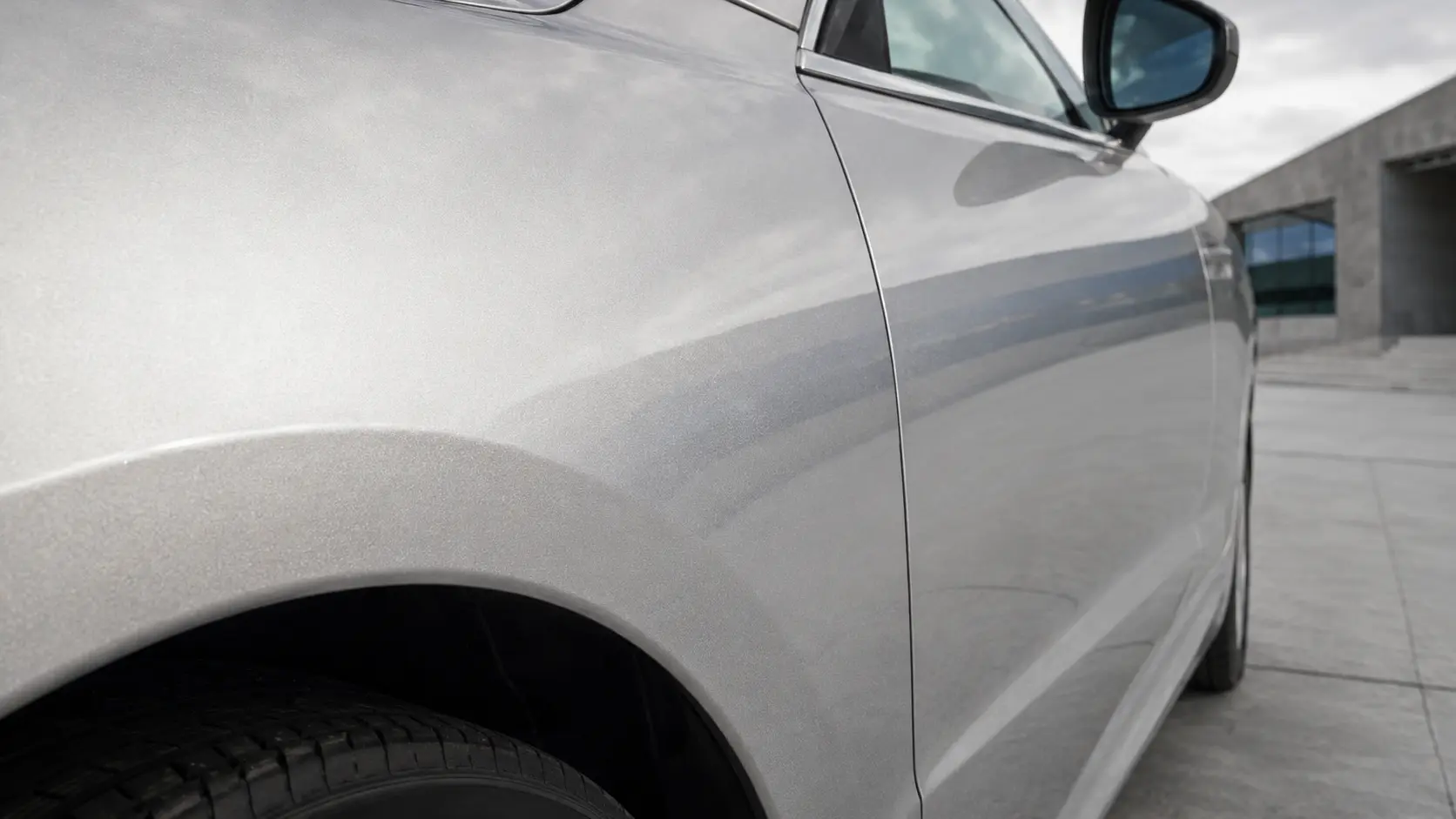 Carrosserie automobile argent métallisé avec fines particules et reflets du ciel sous un jour couvert
