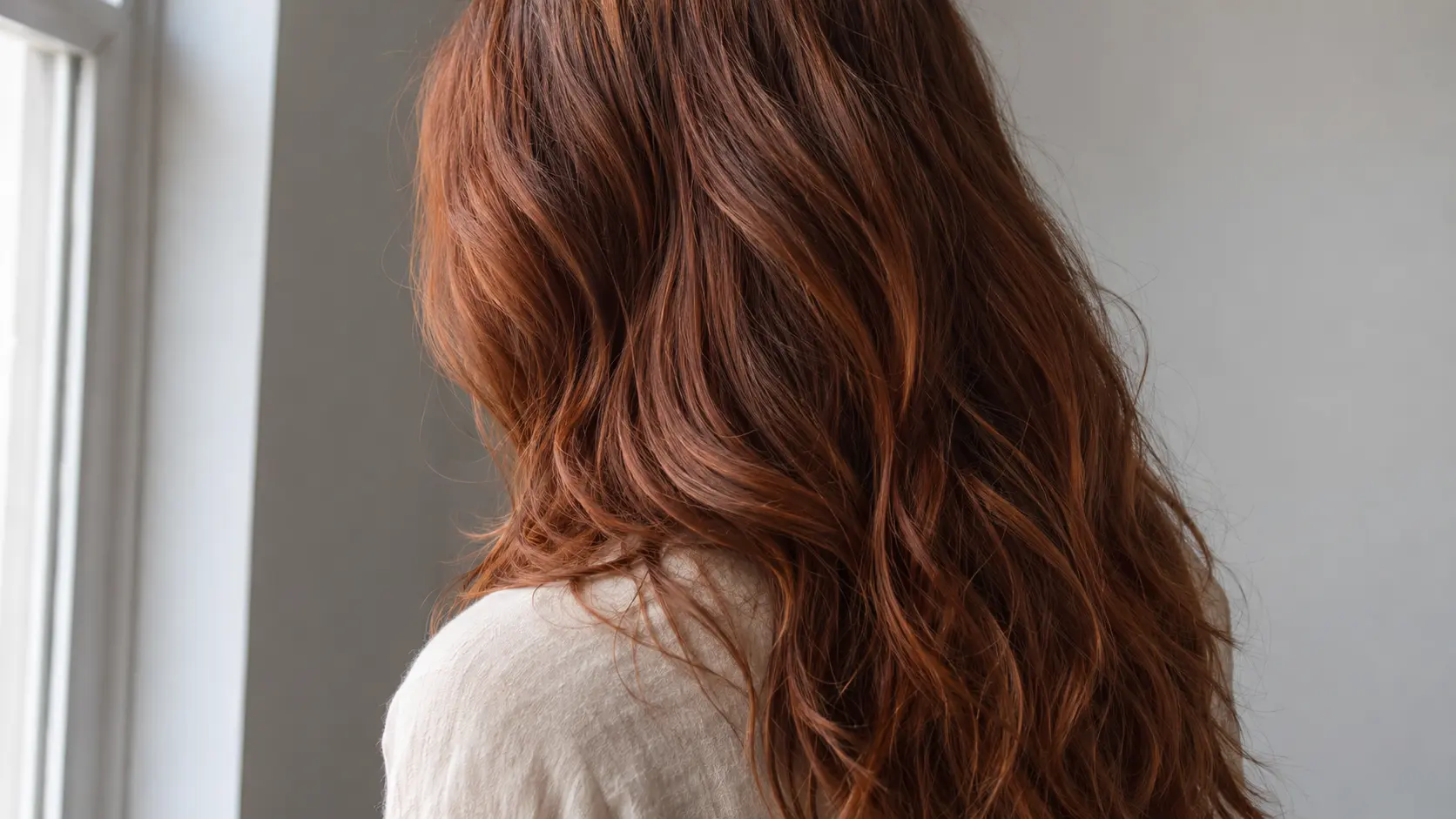 Cheveux longs auburn vus de dos avec base brun rouge et reflets cuivrés sous une lumière naturelle