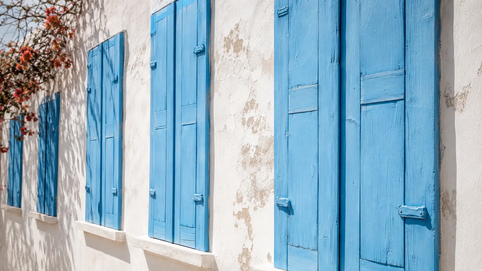Rangée de volets en bois azur sur une façade méditerranéenne blanche patinée