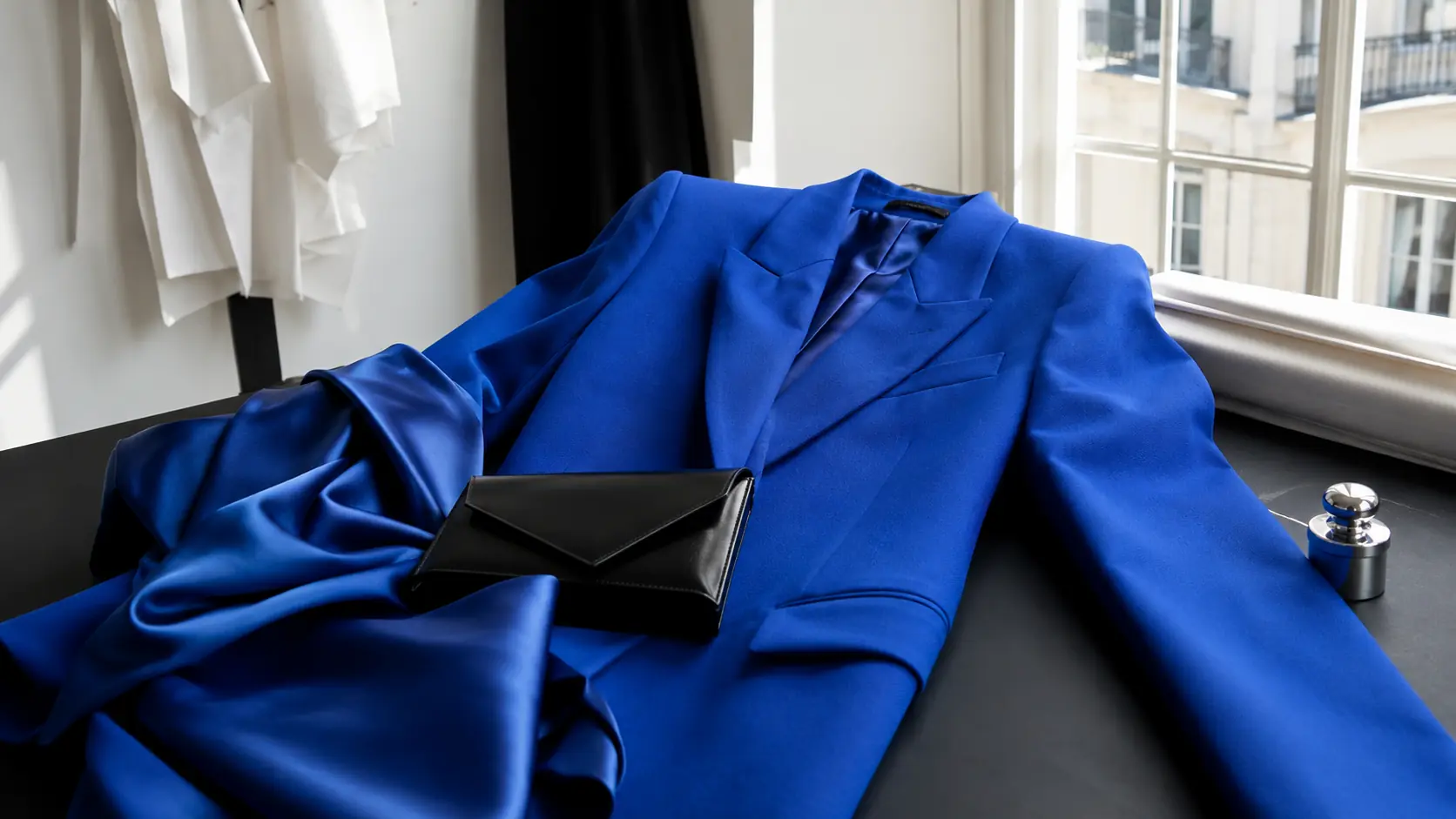 Veste de soirée bleu roi, étoffe satinée et pochette noire photographiées dans un atelier parisien