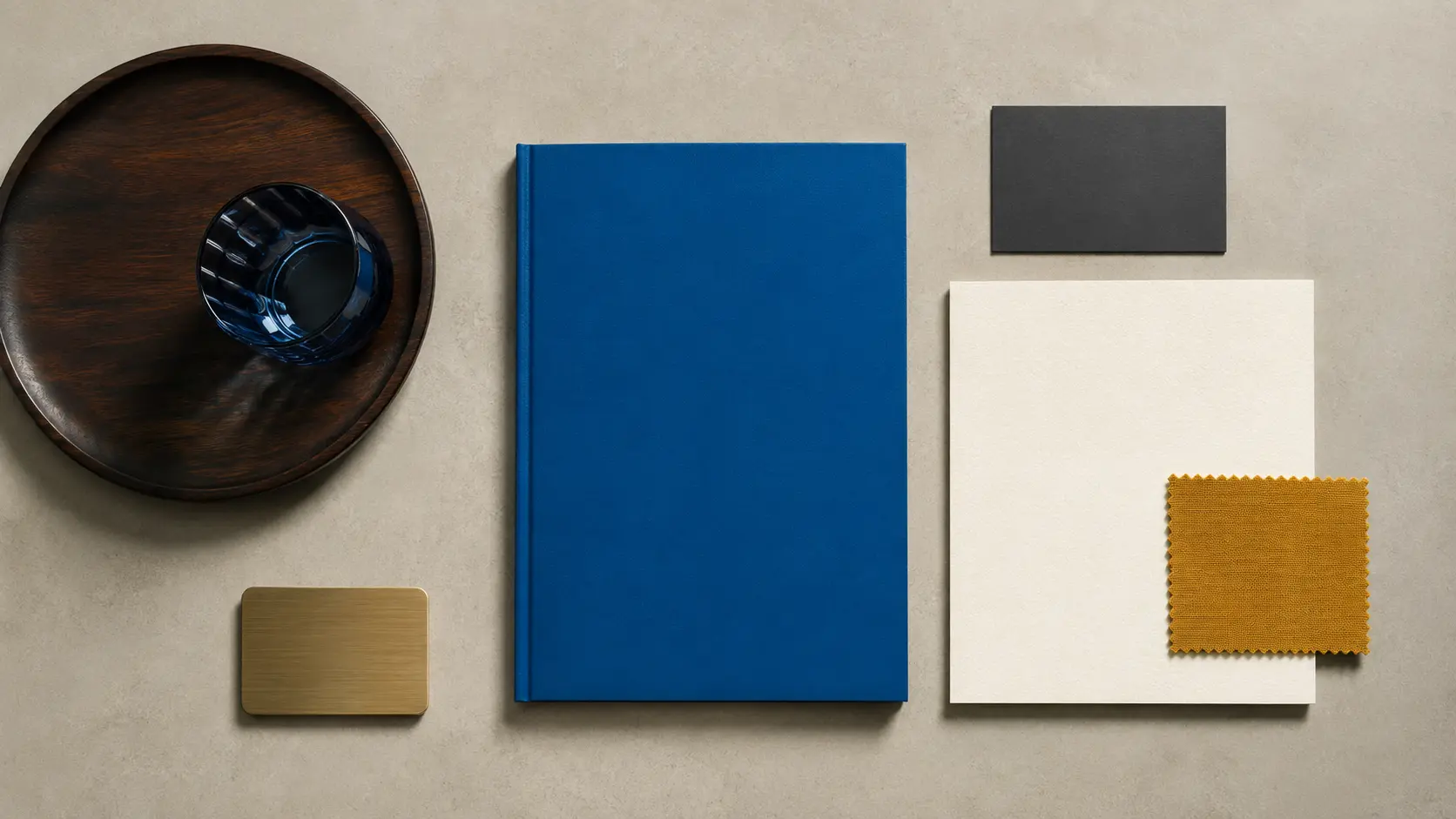 Palette d’application bleu avec carnet bleu, papiers blanc cassé et charbon, ocre jaune, laiton, verre et bois sombre
