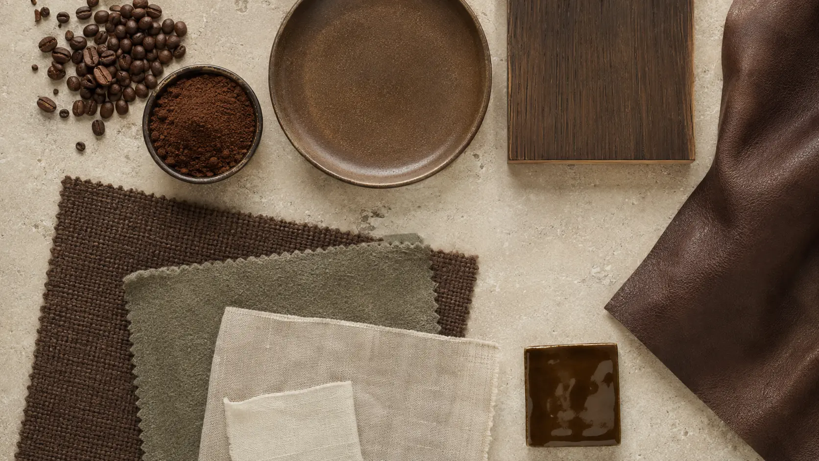 Étude de matières café réunissant grains torréfiés, mouture, céramique mate et brillante, chêne sombre, cuir brun, laine, lin et textile sauge