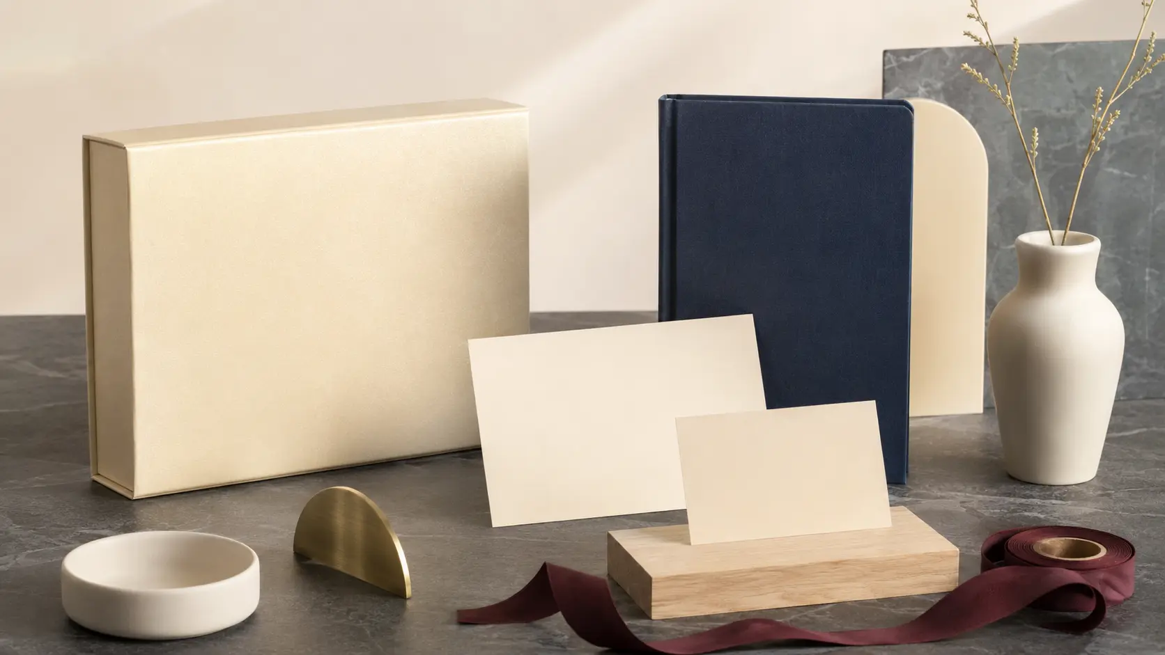 Système d’application champagne avec boîte nacrée sans marque, cartes vierges, carnet bleu nuit, ruban bourgogne, céramique ivoire, chêne clair, pierre charbon et détail métallique brossé
