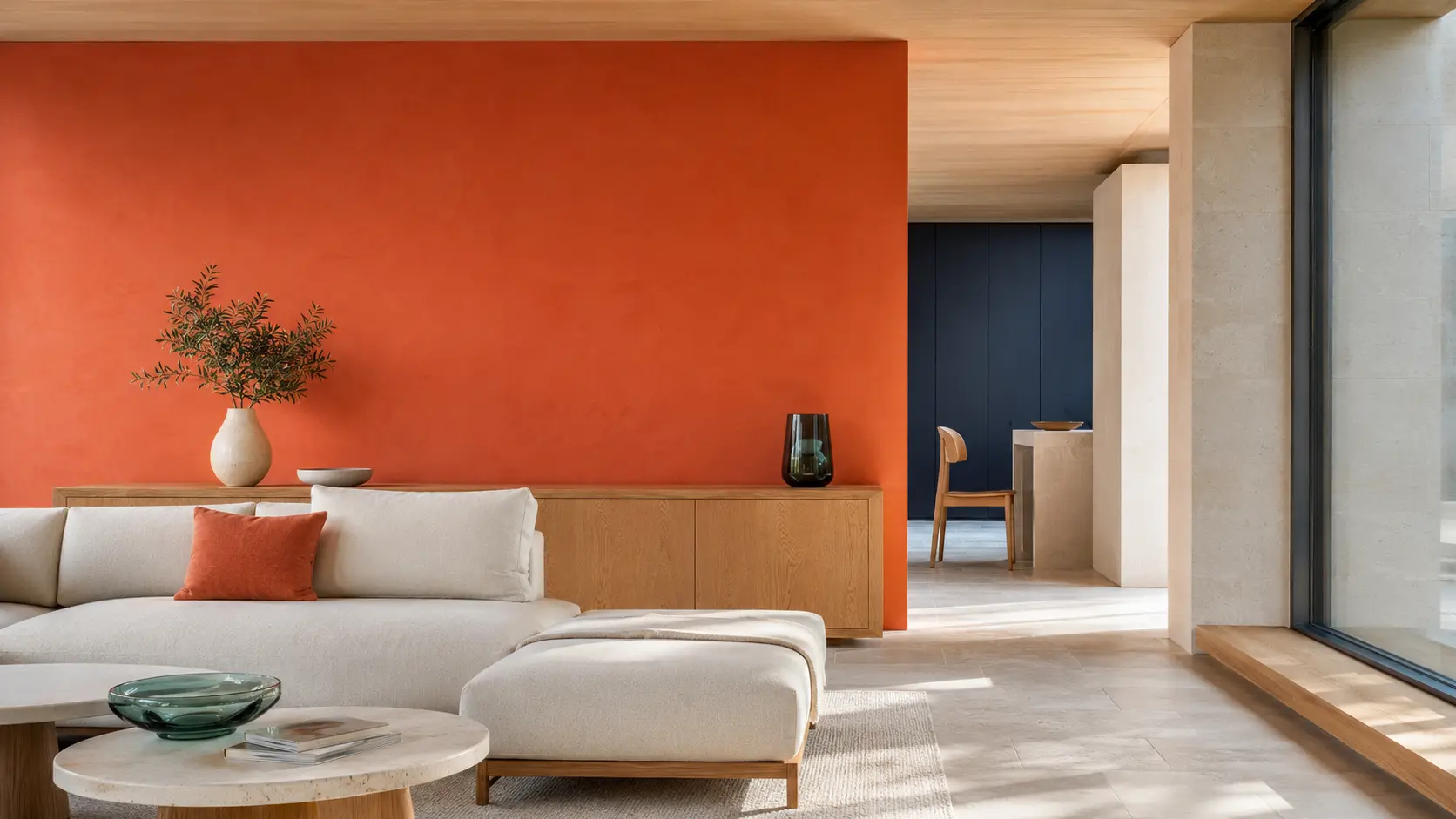 Salon contemporain avec grand mur en enduit corail, pierre coquille claire, mobilier en chêne blond, canapé ivoire, alcôve bleu nuit et objets en verre vert d’eau