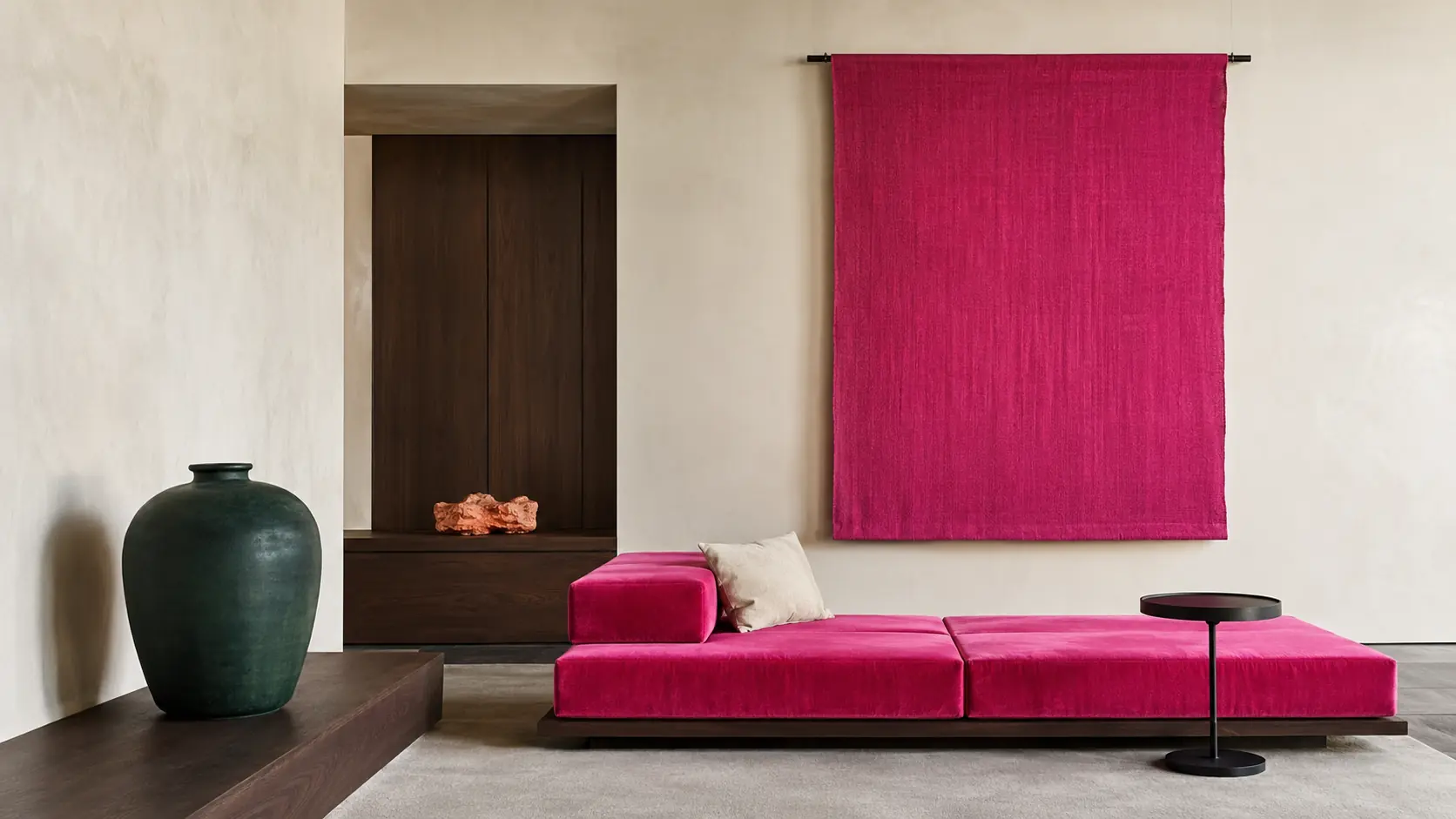 Intérieur contemporain lumineux avec une banquette en velours fuchsia, panneau textile rose violacé, murs en plâtre ivoire, table noire, noyer sombre et grand vase vert profond