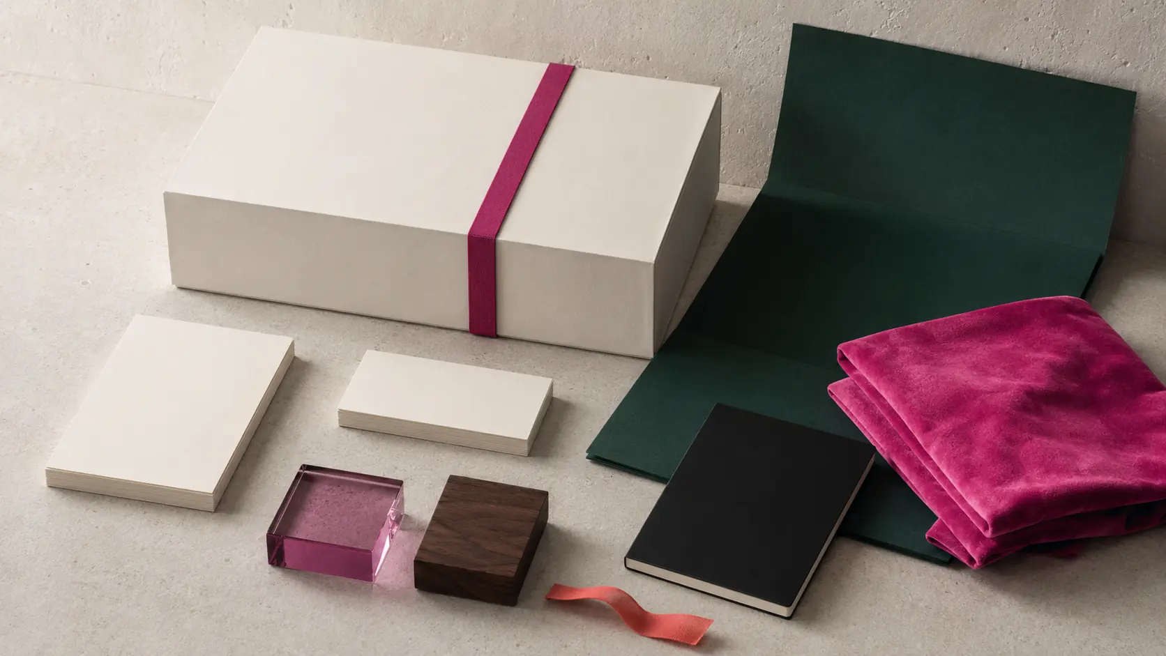 Système d’application fuchsia sans marque avec boîte ivoire à bande rose violacé, cartes vierges, carnet noir, papier vert profond, textile fuchsia, verre teinté et petit ruban corail