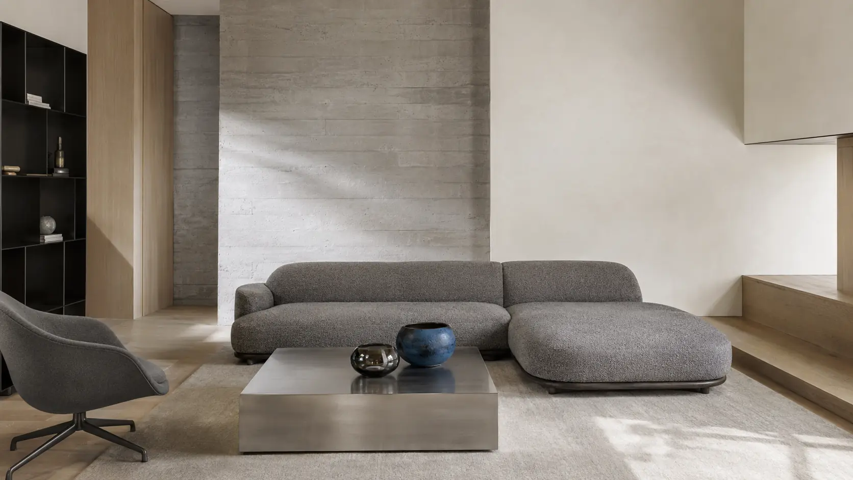 Intérieur contemporain lumineux avec mur en béton gris coffré, canapé en laine grise chinée, panneaux de frêne clair, table en acier brossé, éléments graphite et petit objet bleu minéral