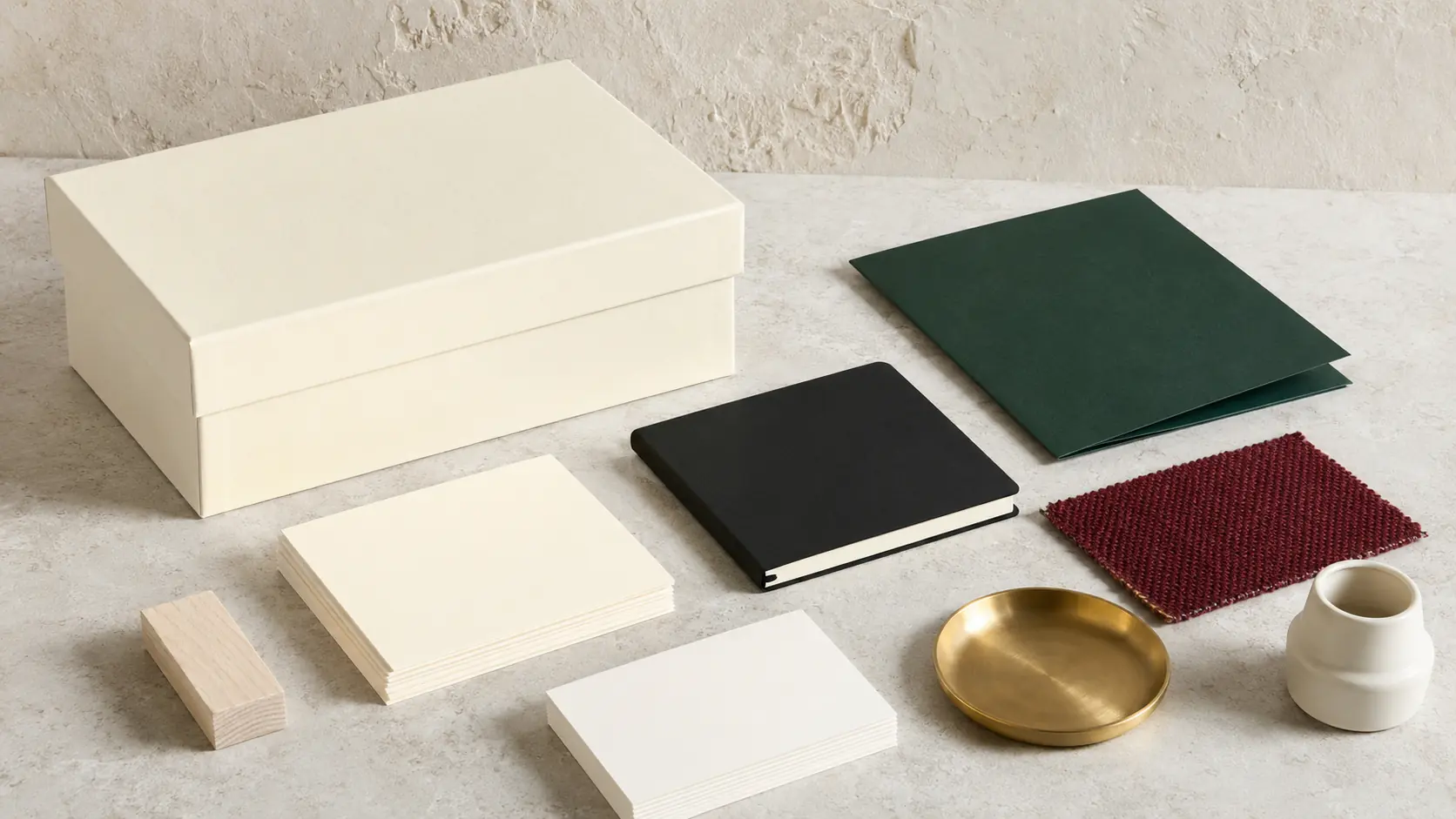 Système d’application ivoire sans marque avec boîte claire, cartes vierges, carnet encre, papier vert profond, textile bordeaux, plaque en laiton doux, porcelaine et petit bloc de frêne