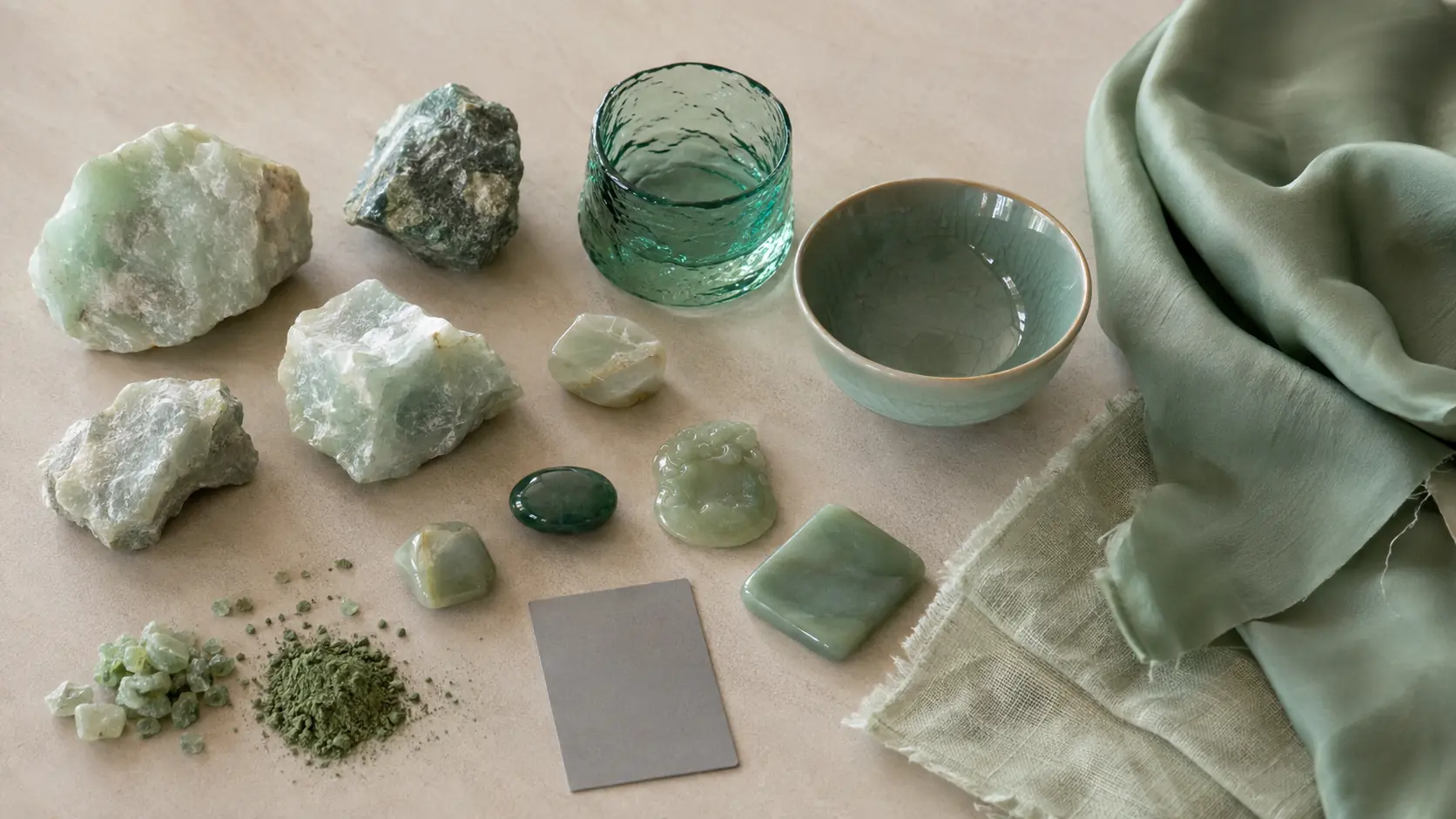 Étude de matières jade réunissant fragments minéraux vert pâle, pierres polies translucides, verre vert, bol céladon, soie, lin, pigment en poudre et carte gris neutre