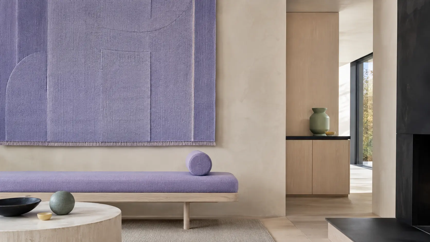 Intérieur contemporain lumineux avec grand panneau textile bleu-violet lavande, banquette lavande, murs crème à la chaux, menuiseries en frêne clair, éléments noir encre