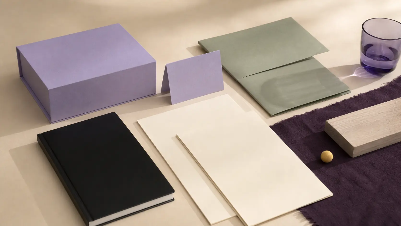 Système d’application lavande sans marque avec boîte et carte lavande, papiers crème vierges, carnet noir encre, chemise sauge, textile prune, verre violet