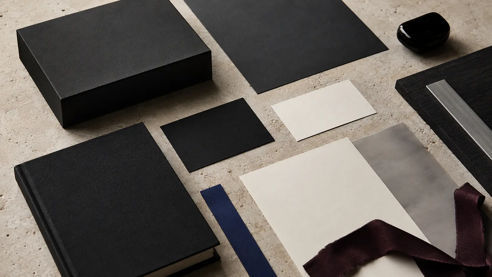 Système d’identité sans marque avec boîte et cartes noires, papiers blanc chaud vierges, carnet en lin noir, feuille gris fumé translucide, accent bleu cobalt, ruban bordeaux sombre