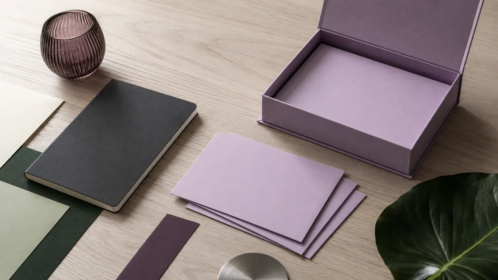 Système d’identité sans marque avec boîte et cartes parme vierges, papiers ivoire, carnet anthracite, feuilles vert forêt et sauge, bande prune fumée, verre violet