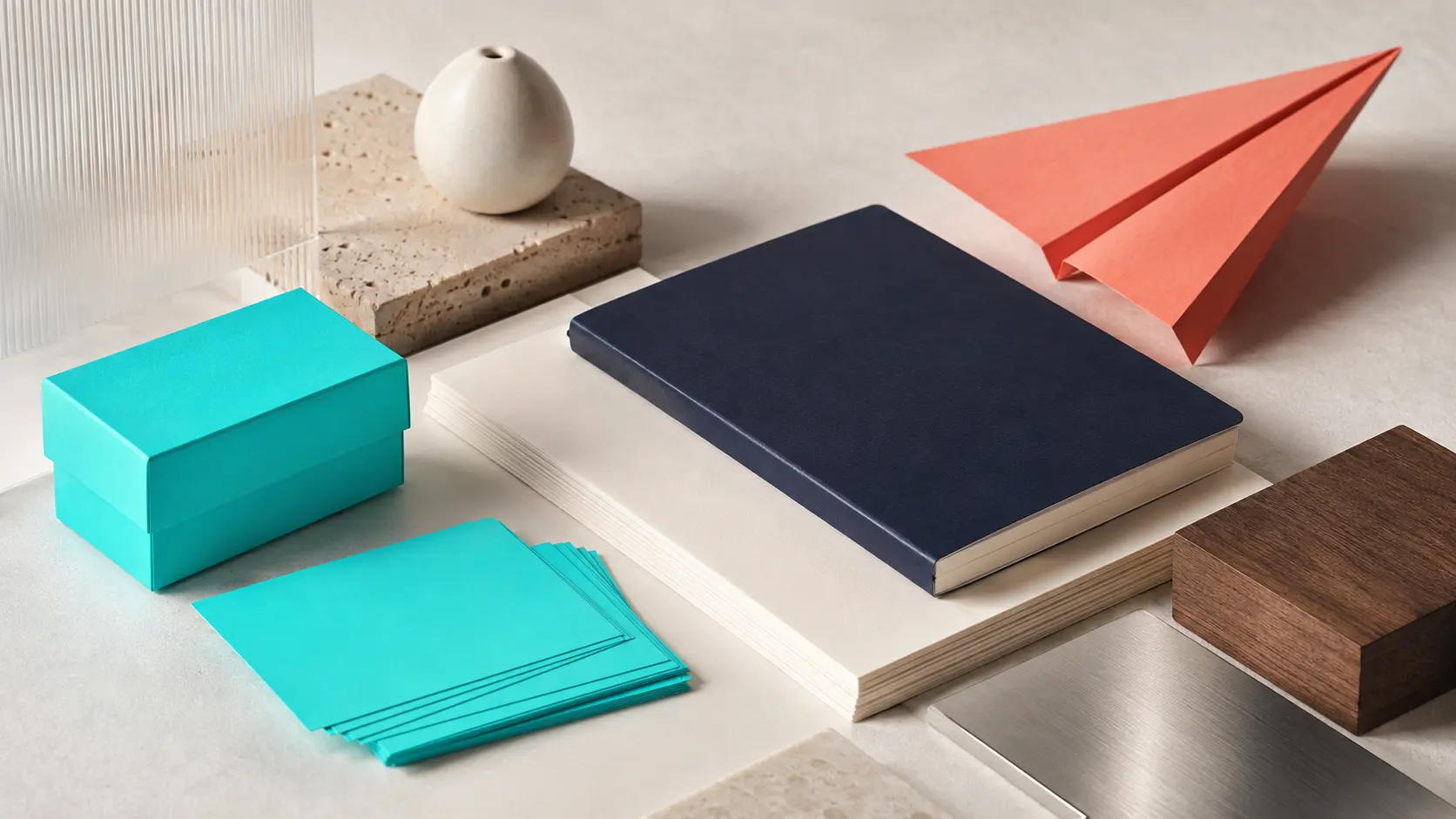 Système d’identité sans marque avec boîte et cartes turquoise vierges, papiers blanc cassé, carnet marine, grande feuille corail, noyer, grès clair, verre dépoli et métal brossé